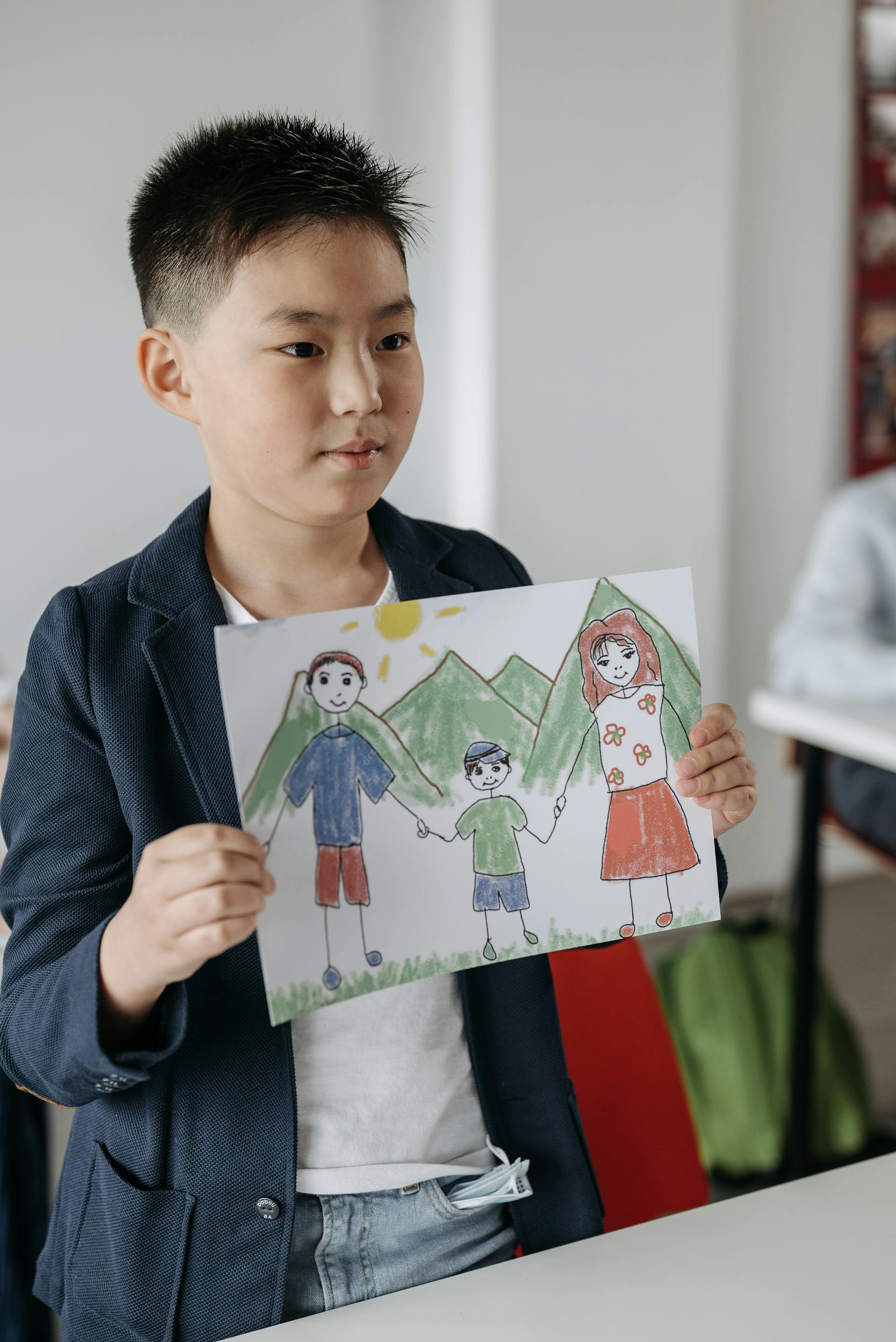 Young Asian boy proudly presenting his drawing in class — speaking with confidence
